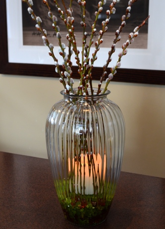 A candle is added to a vase filled with pussy willows.