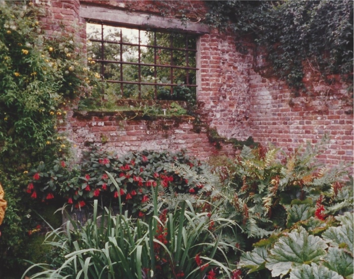A window in an old brick wall which separates two gardens at Sissinghurst.